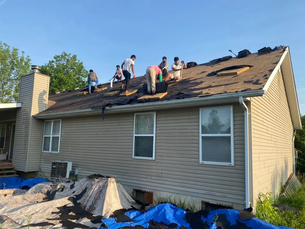 Ranch Roof Tear Off Crew Roofing crew tearing off shingles on the rear slope of a ranch home.