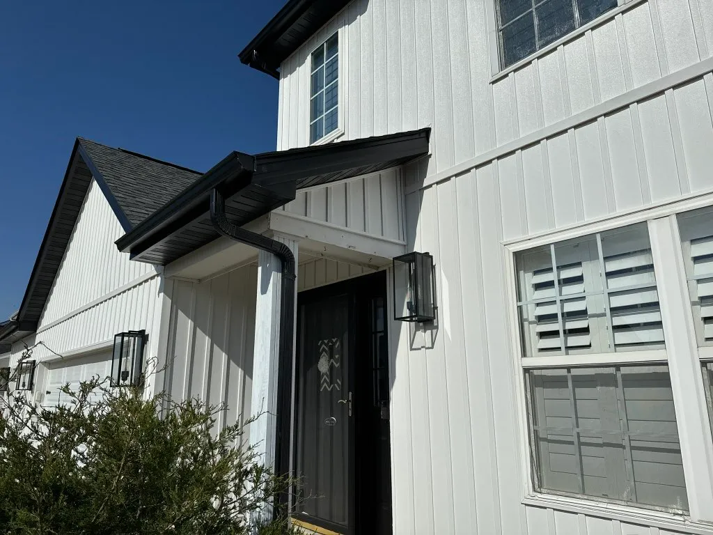 Close exterior view of black gutters and shingle roof on a white home.
