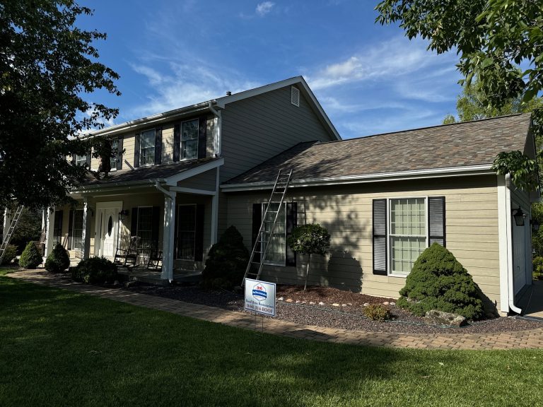 roof bros restoration completed roof 004 - Roof Bros Restoration - roofing gallery wisconsin illinois A two-story house with tan siding, a covered front porch, a newly shingled dark grey roof, and a Roof Bros Restoration yar...