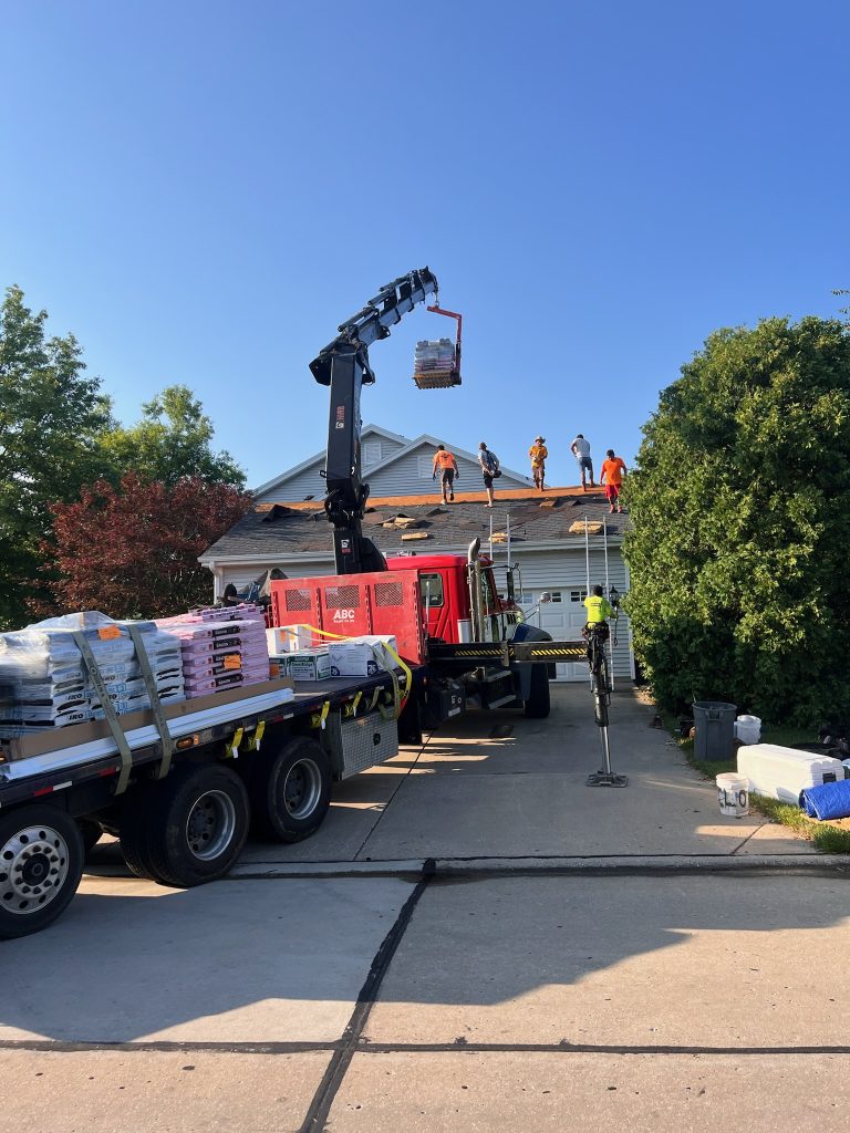 roof bros restoration illinois roof install 001 - Roof Bros Restoration - roofing gallery wisconsin illinois A crane-equipped delivery truck hoists pallets of roofing shingles up to a crew of workers in orange and yellow shirts sta...