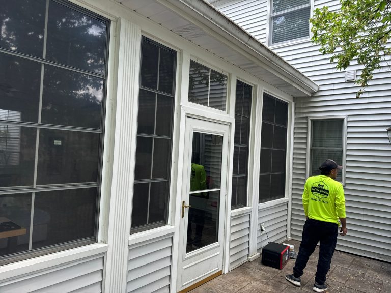roof bros restoration jobsite 005 - Roof Bros Restoration - roofing gallery wisconsin illinois A worker in a Roof Bros yellow safety shirt stands beside a sunroom addition on a white-sided two-story home