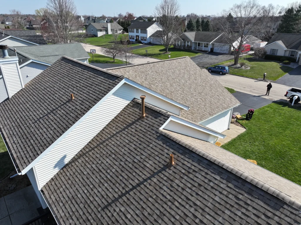 roof bros restoration madison roof replacement drone completed multi section 107 - Roof Bros Restoration - Madison roofing Drone view of a completed multi-section shingle roof with stand-up vent boots and the neighborhood beyond — Madison, WI