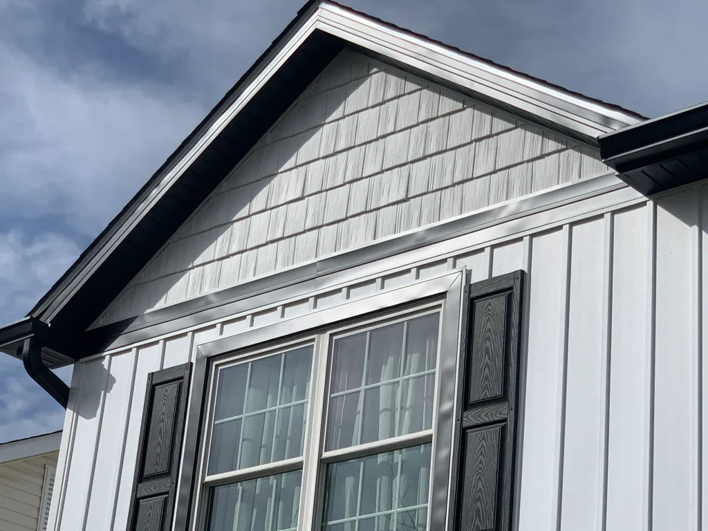 Close-up of a freshly installed white board-and-batten and shingled vinyl gable with black shutters