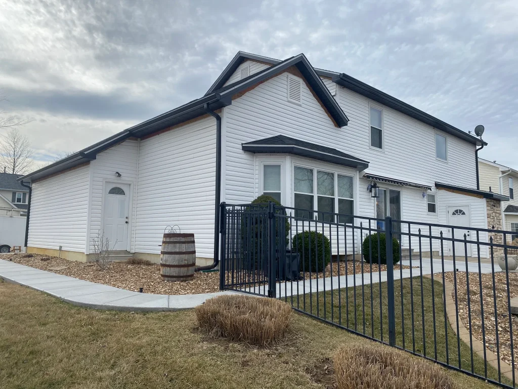 Side and front view of a multi-level home with new white vinyl siding and black gutters