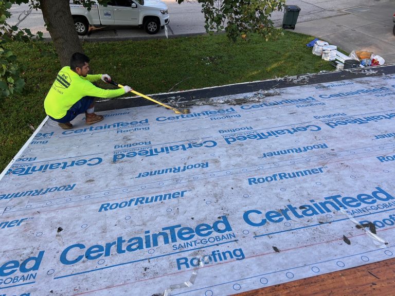 roof bros restoration roof install 001 - Roof Bros Restoration - roofing gallery wisconsin illinois A worker in a yellow safety shirt kneels on a low-slope roof installing CertainTeed RoofRunner synthetic underlayment