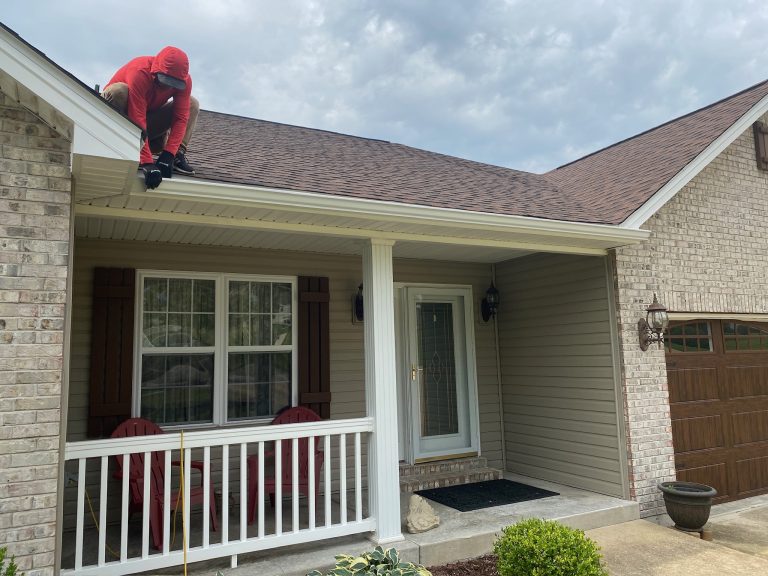 roof bros restoration roof repair 001 - Roof Bros Restoration - roofing gallery wisconsin illinois A worker in a red hoodie kneels at the edge of a shingled roof over a covered porch on a brick-and-siding home