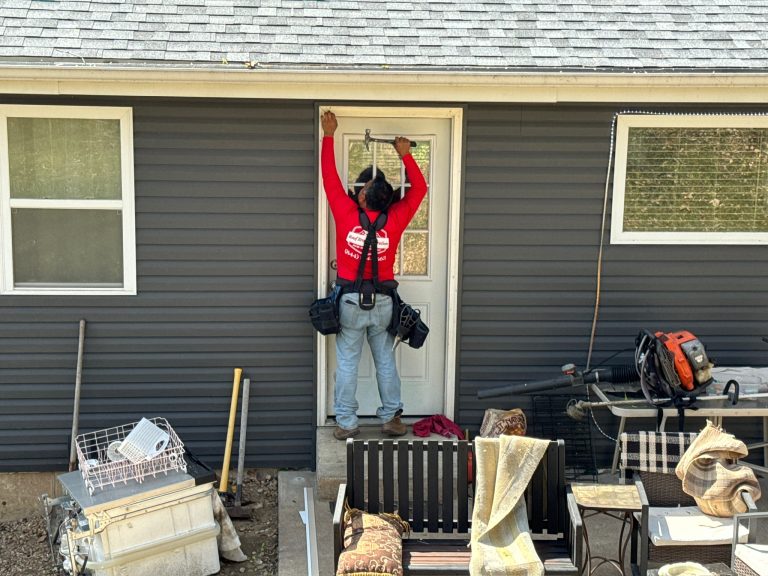 roof bros restoration siding install 002 2 - Roof Bros Restoration - roofing gallery wisconsin illinois A worker in a red Roof Bros Restoration t-shirt and tool belt stands on a back patio installing or repairing trim above a...