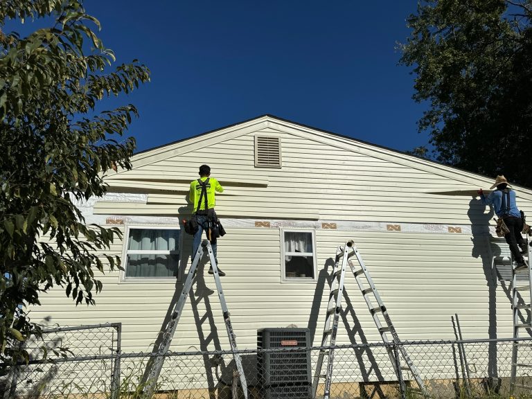 roof bros restoration siding install 003 - Roof Bros Restoration - roofing gallery wisconsin illinois Two workers in yellow-green high-visibility shirts on ladders working on the gable end of a single-story home with cream-c...