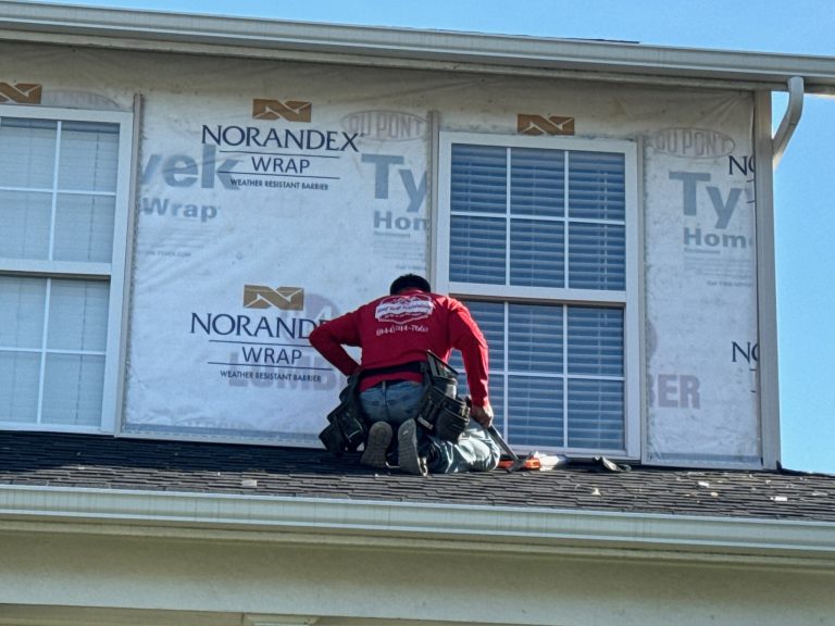 roof bros restoration siding install 005 - Roof Bros Restoration - roofing gallery wisconsin illinois A worker in a red long-sleeve shirt kneeling on a shingled roof installing exterior trim around windows over Norandex weat...