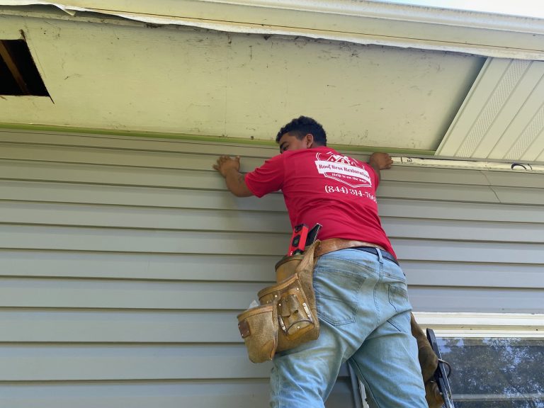 roof bros restoration siding install 009 - Roof Bros Restoration - roofing gallery wisconsin illinois A worker in a red Roof Bros Restoration t-shirt and tool belt stands on a ladder pressing a piece of vinyl siding into pla...