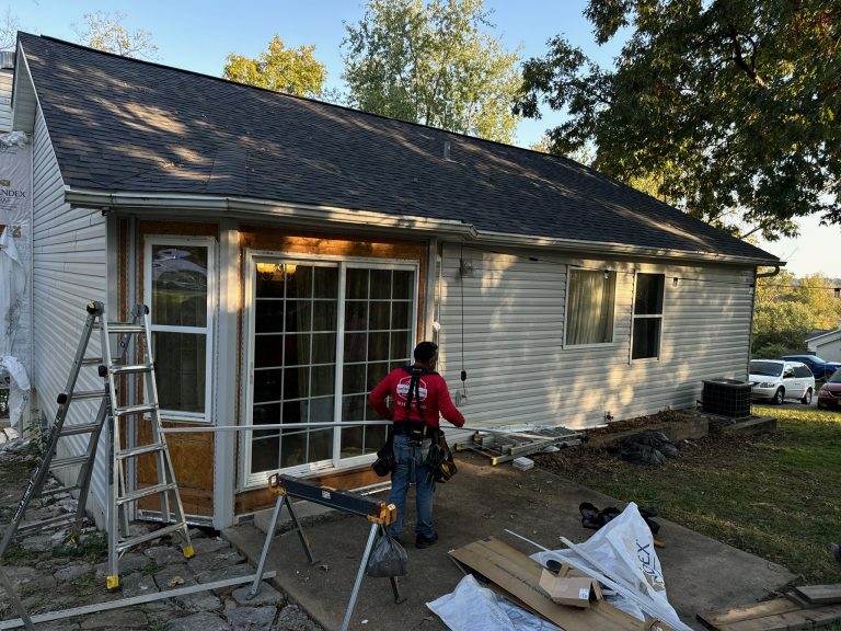 roof bros restoration siding install 010 - Roof Bros Restoration - roofing gallery wisconsin illinois A worker in a red shirt standing in front of a sliding glass patio door on a one-story home with light tan siding, with an...