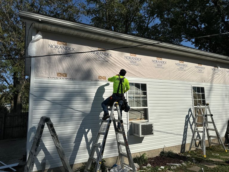 roof bros restoration siding install 011 - Roof Bros Restoration - roofing gallery wisconsin illinois A worker in a yellow-green high-visibility shirt standing on a ladder installing white horizontal vinyl siding over Norand...