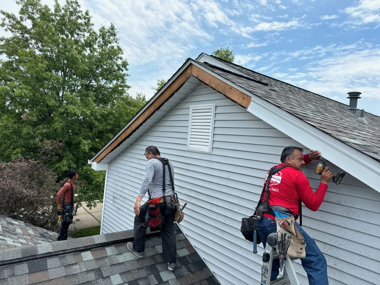 roof bros restoration siding install 012 - Roof Bros Restoration - roofing gallery wisconsin illinois Three workers in red and gray shirts install siding and trim on a gable end of a gray-sided home from the adjoining shingl...