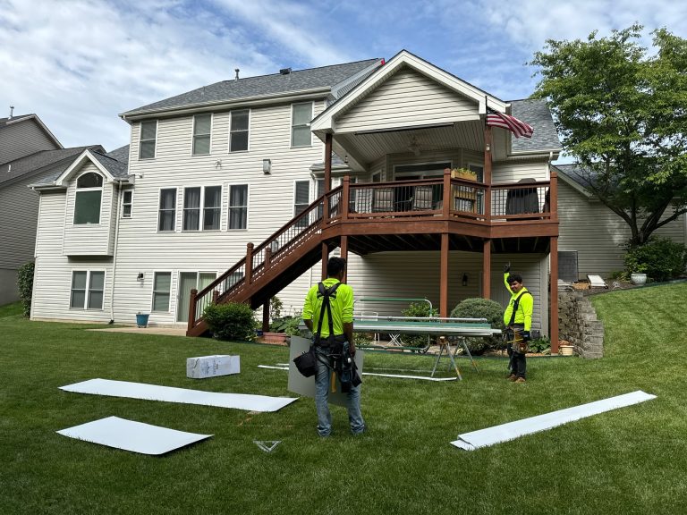 roof bros restoration siding install 013 - Roof Bros Restoration - roofing gallery wisconsin illinois Two workers in high-visibility yellow shirts stand on the back lawn of a tan two-story house with a raised wooden deck, wi...