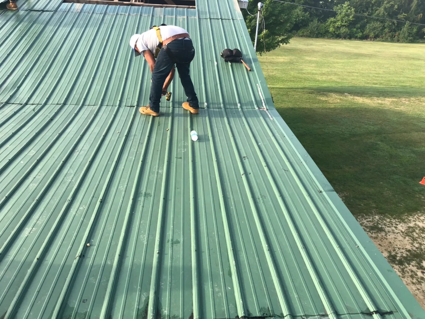 Roof Repair in St. Louis, MO — Roofer Working on a Green Roofer working on a green standing-seam metal roof, sealing panels during repair — St. Louis, MO