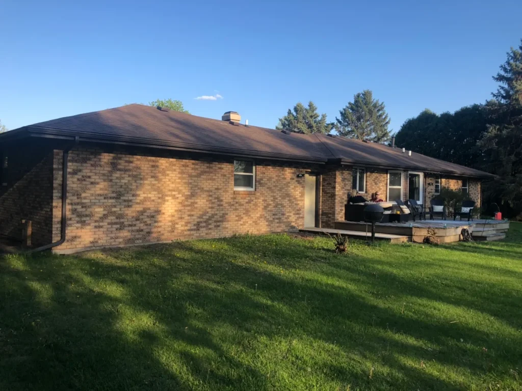 Side view of brick ranch home with finished dark brown asphalt-shingle roof at sunset