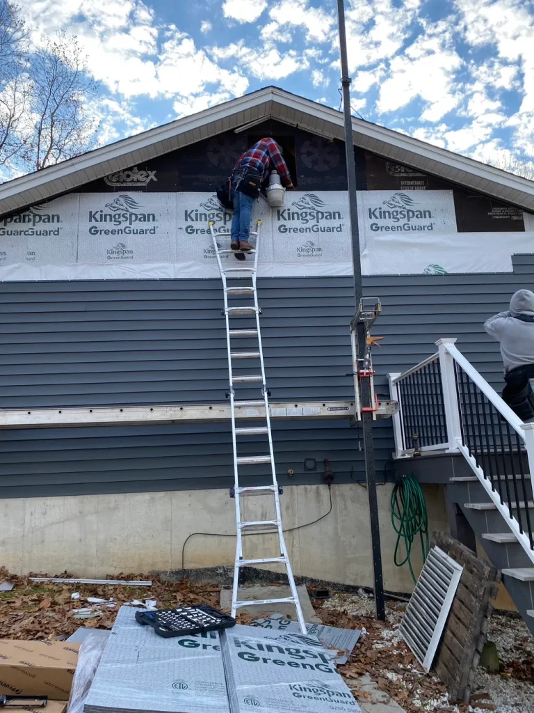 Roofer on a ladder working on a gable wall covered in Kingspan GreenGuard insulation during siding work