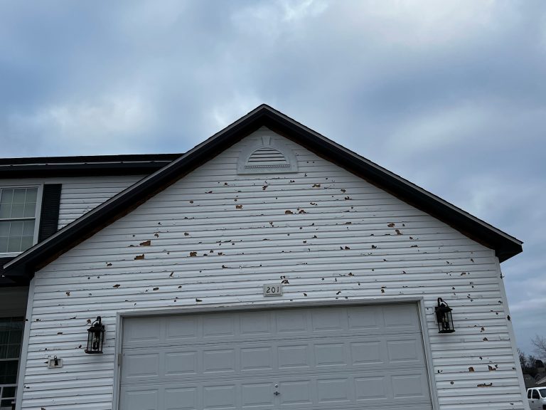 roof bros restoration storm damage 001 - Roof Bros Restoration - roofing gallery wisconsin illinois The gable end of a two-story home with white horizontal vinyl siding showing extensive hail-impact damage as numerous roun...