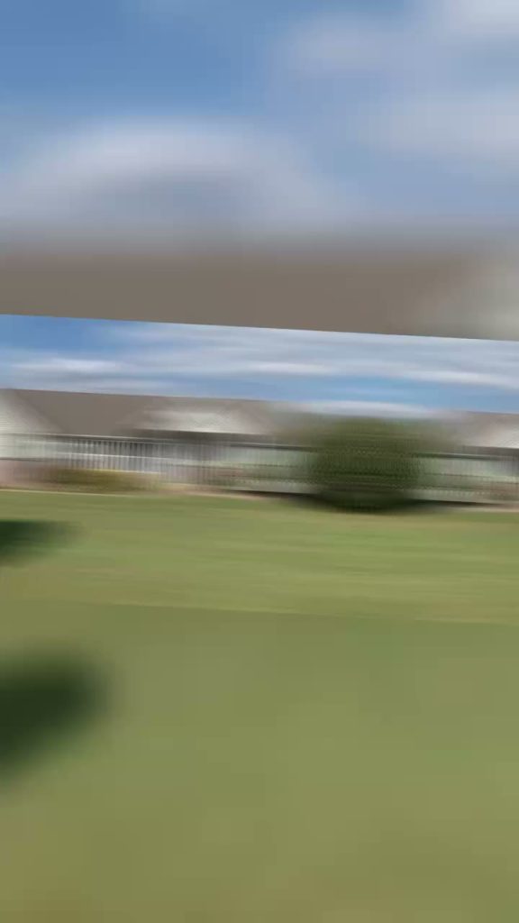 roof bros restoration video poster jobsite 013 - Roof Bros Restoration - roofing gallery wisconsin illinois Motion-blurred drive-by frame showing a long single-story building with a fence and open lawn under a partly cloudy sky