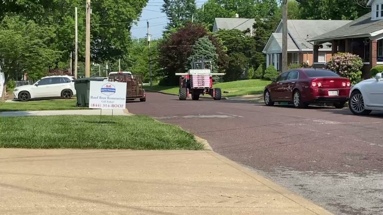 roof bros restoration video poster jobsite 014 - Roof Bros Restoration - roofing gallery wisconsin illinois Red Moffett forklift driving down a residential street pulling a trailer, with a Roof Bros Restoration yard sign on a corn...