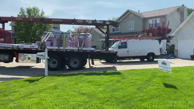 roof bros restoration video poster jobsite 016 - Roof Bros Restoration - roofing gallery wisconsin illinois Red ABC Supply flatbed truck loaded with shingle bundles parked at curb with a white work van and two-story suburban homes...