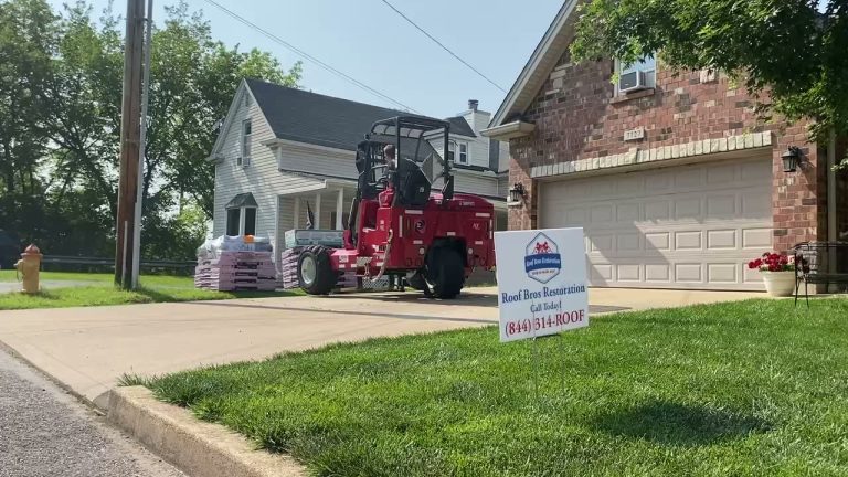 roof bros restoration video poster jobsite 017 - Roof Bros Restoration - roofing gallery wisconsin illinois Red Moffett forklift parked in a residential driveway near pallets of shingle bundles, with a Roof Bros Restoration yard s...