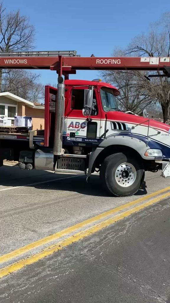 roof bros restoration video poster jobsite 019 - Roof Bros Restoration - roofing gallery wisconsin illinois Close-up side view of a red and white ABC Supply Mack delivery truck with WINDOWS and ROOFING labeled on its conveyor boom...