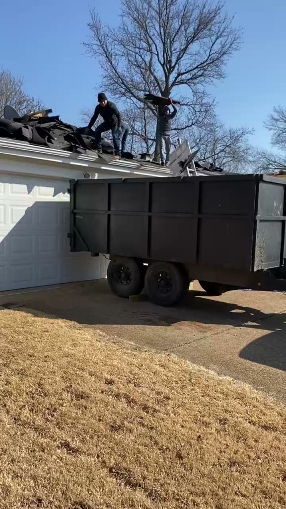 roof bros restoration video poster roof install 005 - Roof Bros Restoration - roofing gallery wisconsin illinois Two workers tearing off old shingles on a roof and tossing debris into a black dump trailer parked in front of a white gar...