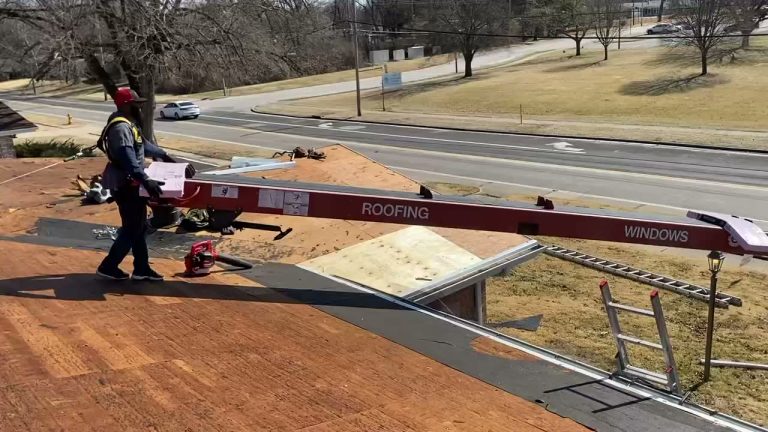 roof bros restoration video poster roof install 006 - Roof Bros Restoration - roofing gallery wisconsin illinois Worker on a rooftop next to an extended red conveyor labeled ROOFING and WINDOWS, with a residential street, leafless tree...