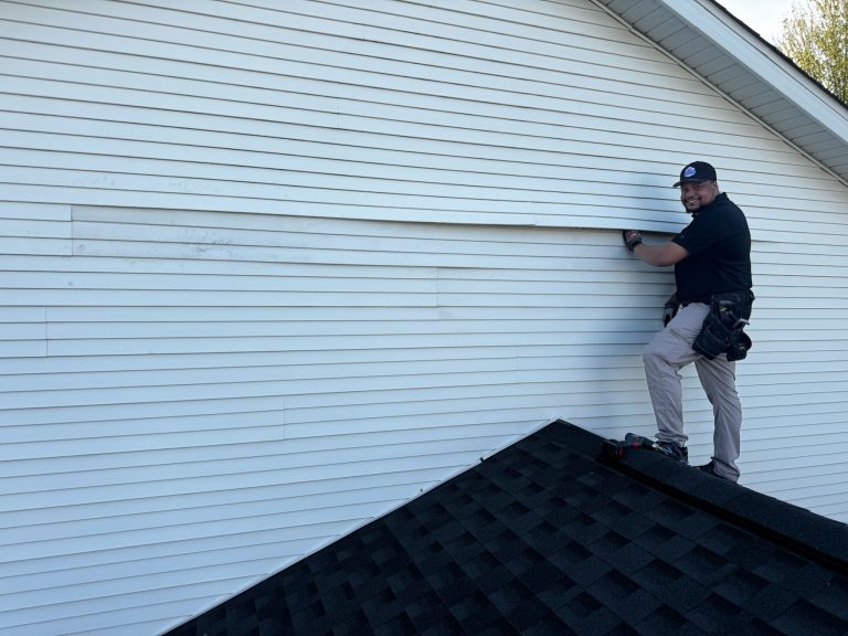 roof bros restoration wisconsin siding install 001 - Roof Bros Restoration - roofing gallery wisconsin illinois A smiling worker in a black cap and black polo shirt stands on a shingled roof slope installing horizontal white vinyl sid...