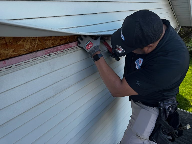 roof bros restoration wisconsin siding install 002 - Roof Bros Restoration - roofing gallery wisconsin illinois A worker in a black cap, black polo, and work gloves uses a tool to fit a piece of white vinyl siding into the J-channel b...