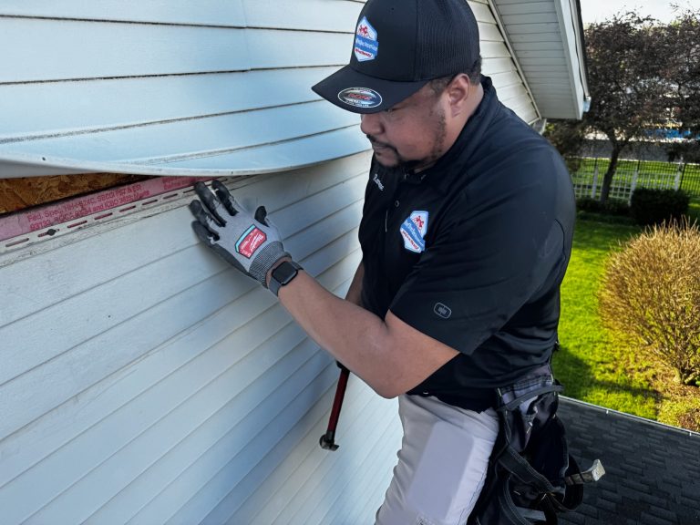 roof bros restoration wisconsin siding install 003 - Roof Bros Restoration - roofing gallery wisconsin illinois A worker in a black Roof Bros Restoration branded cap and polo shirt fastens white vinyl siding to a wall with exposed OSB...