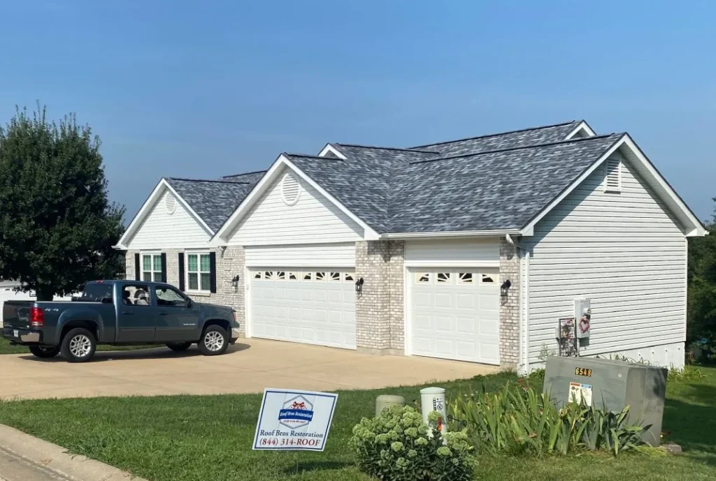 White ranch home with a newly shingled gray roof, an attached three-car garage and a Roof Bros Restoration yard sign out front